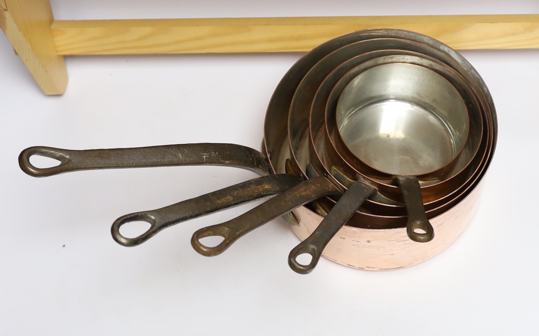 A graduated set of five French copper pans and a pine hanging rack